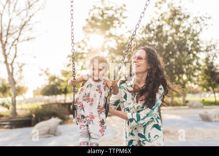 Felice madre spingendo carino figlia swinging presso il parco giochi Foto Stock