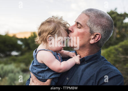 Close-up di padre baciare sulla figlia di fronte mentre in piedi contro il cielo in foresta Foto Stock