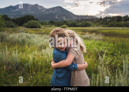Felice sorelle abbracciando mentre si sta in piedi sul campo erboso nella foresta durante il tramonto Foto Stock