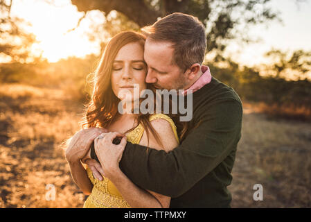 Il marito abbracciando la moglie mentre nel campo della California durante il tramonto Foto Stock