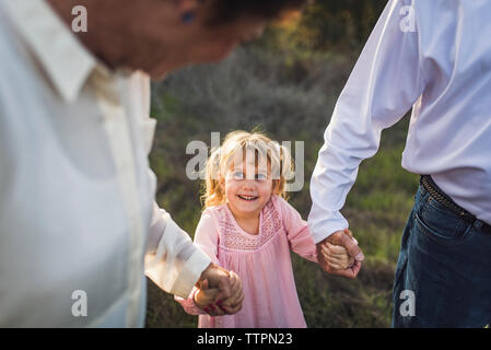 Bambina tenendo le mani con i nonni, guardando verso l'alto e sorridente Foto Stock