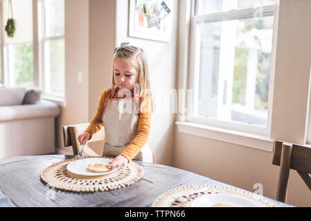 Bambina con grembiule flipping pancake al tavolo per la colazione Foto Stock
