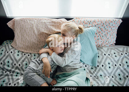 Angolo di Alta Vista della sorella kissing fratello mentre giaceva sul letto di casa Foto Stock