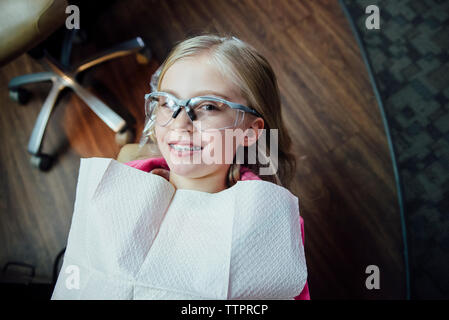 Angolo alto ritratto della ragazza con bretelle seduta a dentisti office Foto Stock