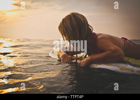 Donna sdraiata sulla tavola da surf in mare contro sky Foto Stock