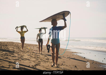 Gli amici che trasportano le tavole da surf mentre passeggiate in spiaggia contro sky Foto Stock