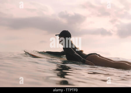 Donna surf sul mare contro il cielo nuvoloso durante il tramonto Foto Stock