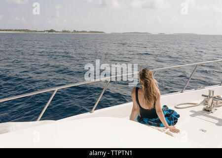 Vista posteriore della donna che guarda al mare durante un viaggio in barca contro sky durante la giornata di sole Foto Stock