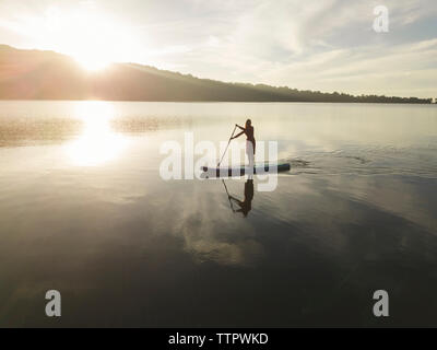 Una femmina paddleboarding su un lago di sunrise Foto Stock