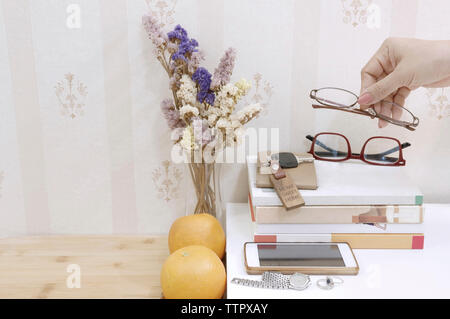 Ritagliato mano azienda occhiali dal vaso di fiori a tavola Foto Stock