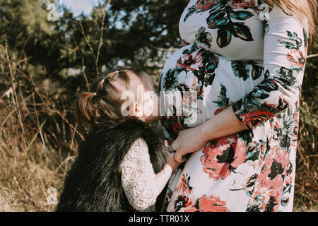 Amorevole figlia kissing in stato di gravidanza della madre pancia mentre si sta in piedi in foresta Foto Stock