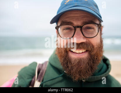 Close-up ritratto di sorridente uomo barbuto che indossa il cappello e occhiali a beach Foto Stock
