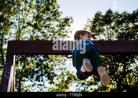 Basso angolo vista del ragazzo swinging contro sky nel parco giochi Foto Stock