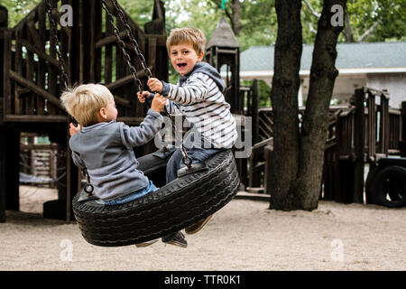 Felice fratelli godendo il tire swing nel parco giochi Foto Stock