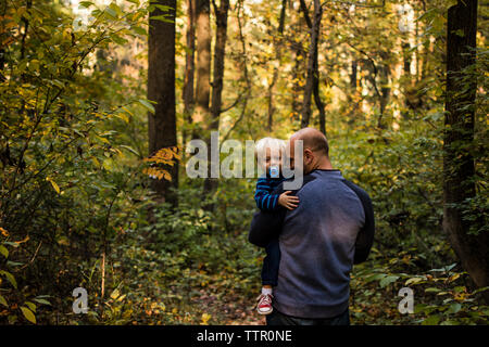 Padre che porta il figlio mentre sta in piedi nella foresta Foto Stock