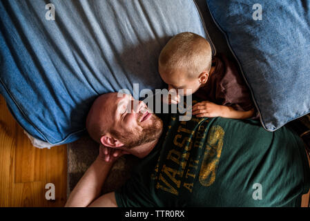 Padre la posa sul pavimento su dei cuscini e sorridente al figlio che stabilisce con lui Foto Stock