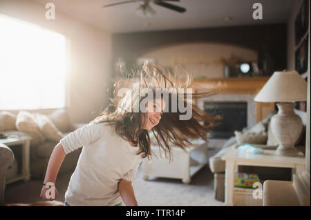 Sorridente ragazza lanciando capelli mentre in piedi in salotto Foto Stock