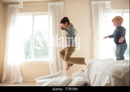 Fratello avendo divertimento salta fuori bed in cuscini in camera da letto Foto Stock