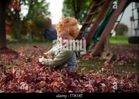 Sweet toddler boy sorrisi durante la riproduzione in foglie in cortile Foto Stock