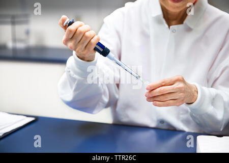 Femmina senior scientist chimica di colata attraverso una pipetta in laboratorio Foto Stock