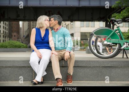 Coppia matura kissing seduti sui gradini in città Foto Stock