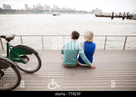 Vista posteriore della coppia matura guardando a vista sulla città mentre è seduto sul lungomare Foto Stock