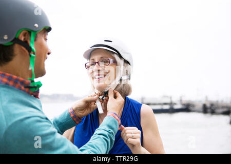 Uomo maturo ad assistere la donna in bicicletta che indossa il casco contro il cielo chiaro Foto Stock