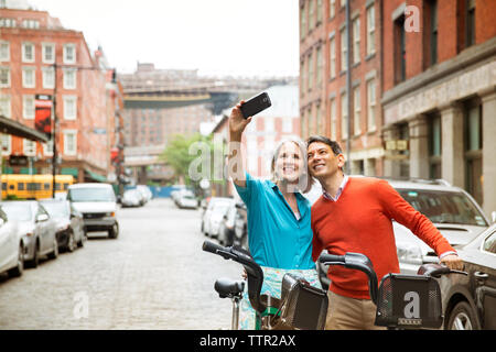 Coppia matura tenendo selfie stando in piedi con le biciclette su strada di città Foto Stock