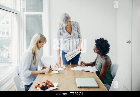 Coppia imprenditrice discutendo sui documenti con i colleghi di sesso femminile nel board camera Foto Stock