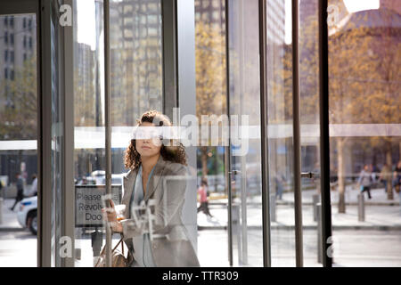 donna d'affari che apre una porta girevole mentre entra in un edificio moderno Foto Stock