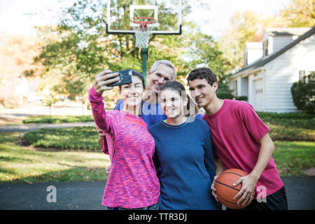 Famiglia tenendo selfie mentre in piedi contro il basket ball hoop a backyard Foto Stock