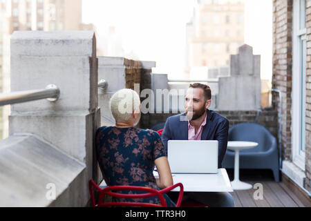 Uomo che utilizza il computer portatile mentre discute con un collega in ufficio balcone Foto Stock