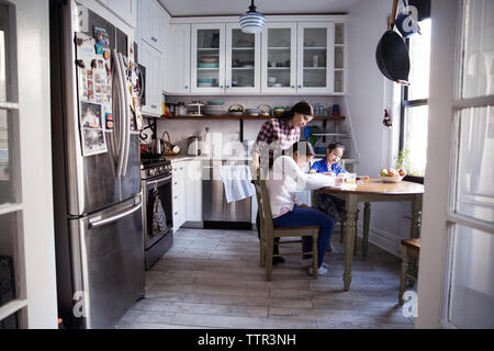 La donna che assiste le figlie per studiare a tavola in cucina Foto Stock