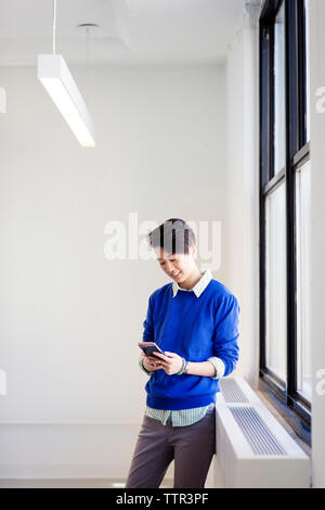 donna d'affari che utilizza il telefono cellulare mentre si trova accanto alla finestra nel nuovo ufficio Foto Stock
