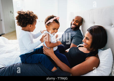 Genitori felici giocando con i bambini durante i momenti di relax sul letto di casa Foto Stock