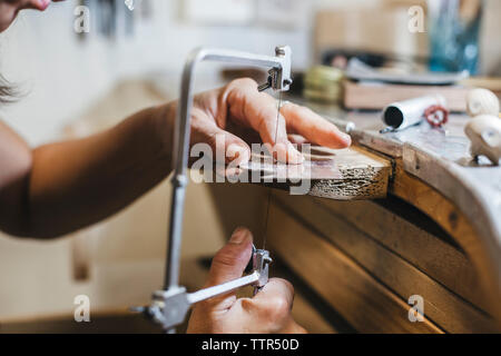 Tagliate le mani di artigiani femmina utilizzando handsaw mentre la gioielleria sul tavolo di legno in officina Foto Stock