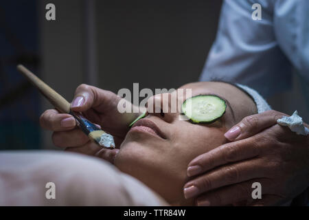 Mani tagliate di estetista di applicare la maschera facciale femmina e il cliente al centro estetico Foto Stock