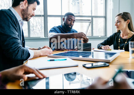 Imprenditrice guardando i colleghi che fissa il cavo per batteria mentre si lavora sul pannello solare modello Foto Stock