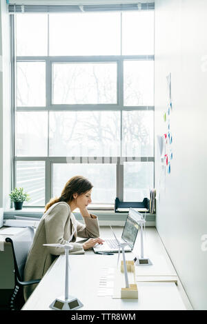 donna d'affari che utilizza un computer portatile mentre è seduta alla scrivania in ufficio Foto Stock