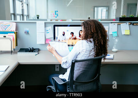 donna d'affari che analizza i documenti durante le videoconferenze con i colleghi in ufficio Foto Stock