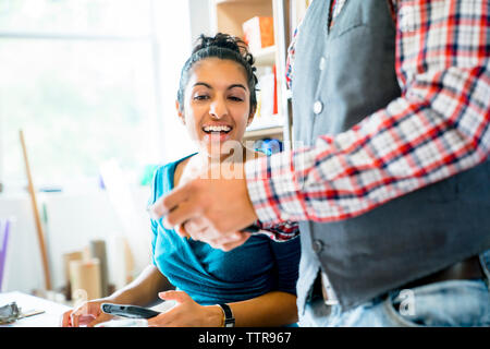 Sezione mediana di imprenditore che mostra smart phone a felice collega femmina in office Foto Stock