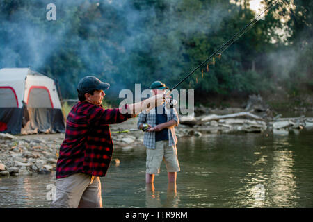 Gli amici di pesca in piedi mentre nel lago durante il tramonto Foto Stock