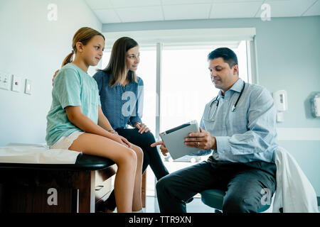 Pediatra discutendo su tablet PC con la madre e la figlia in medical sala esame Foto Stock