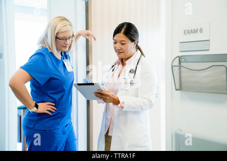 Medici di sesso femminile guardando il computer tablet mentre in piedi dalla parete in ospedale Foto Stock