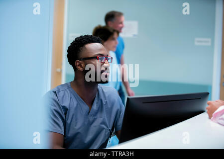 Medico che lavorava alla reception in ospedale con i colleghi in background Foto Stock