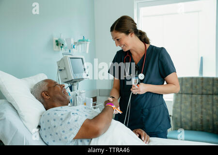 Infermiera sorridente handshaking senior con il paziente sdraiato sul letto in ospedale Foto Stock