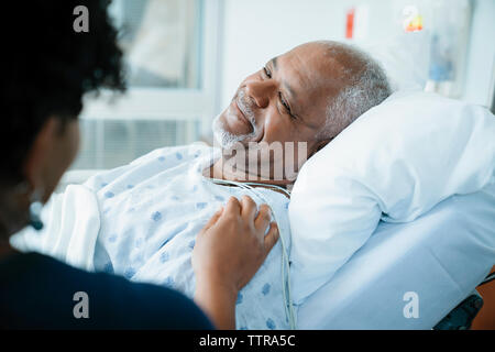 Immagine ritagliata della figlia di toccare padre sdraiato sul letto in ospedale Foto Stock