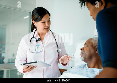 Medico con tablet pc parlando a senior paziente sdraiato dalla figlia in ospedale Foto Stock