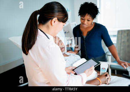 Medico donna guardando il computer tablet mentre si discute con il paziente e la donna in ospedale Foto Stock