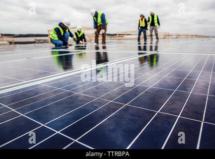 I lavoratori che operano sul pannello solare campo contro il cielo nuvoloso Foto Stock